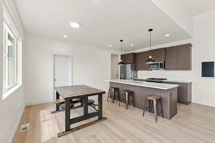 Kitchen featuring wood-finish cabinetry, stainless steel appliances, a center island with counter seating, and light wood-finish flooring