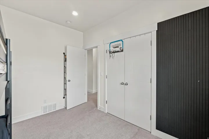 Plush carpet flooring, recessed ceiling lighting, a dark accent wall with vertical paneling, and white bi-fold closet doors