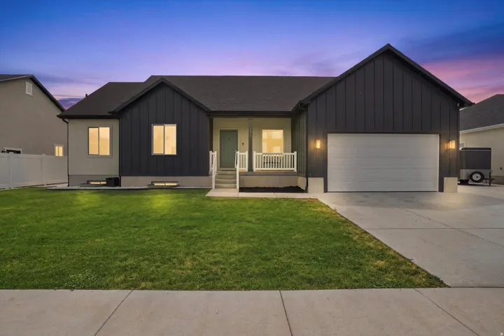 Modern ranch-style home featuring a two-car garage, board and batten siding, a covered porch with white railings, and a manicured front lawn