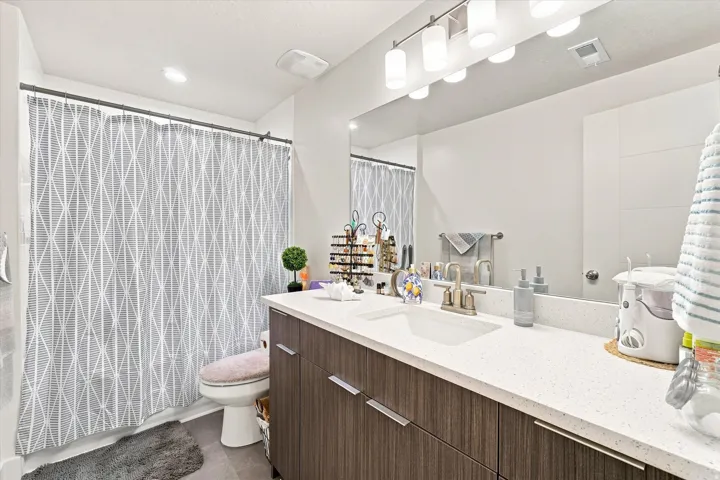 Bathroom vanity with a white countertop and integrated sink, modern wood-finish cabinetry, and a large wall-mounted mirror