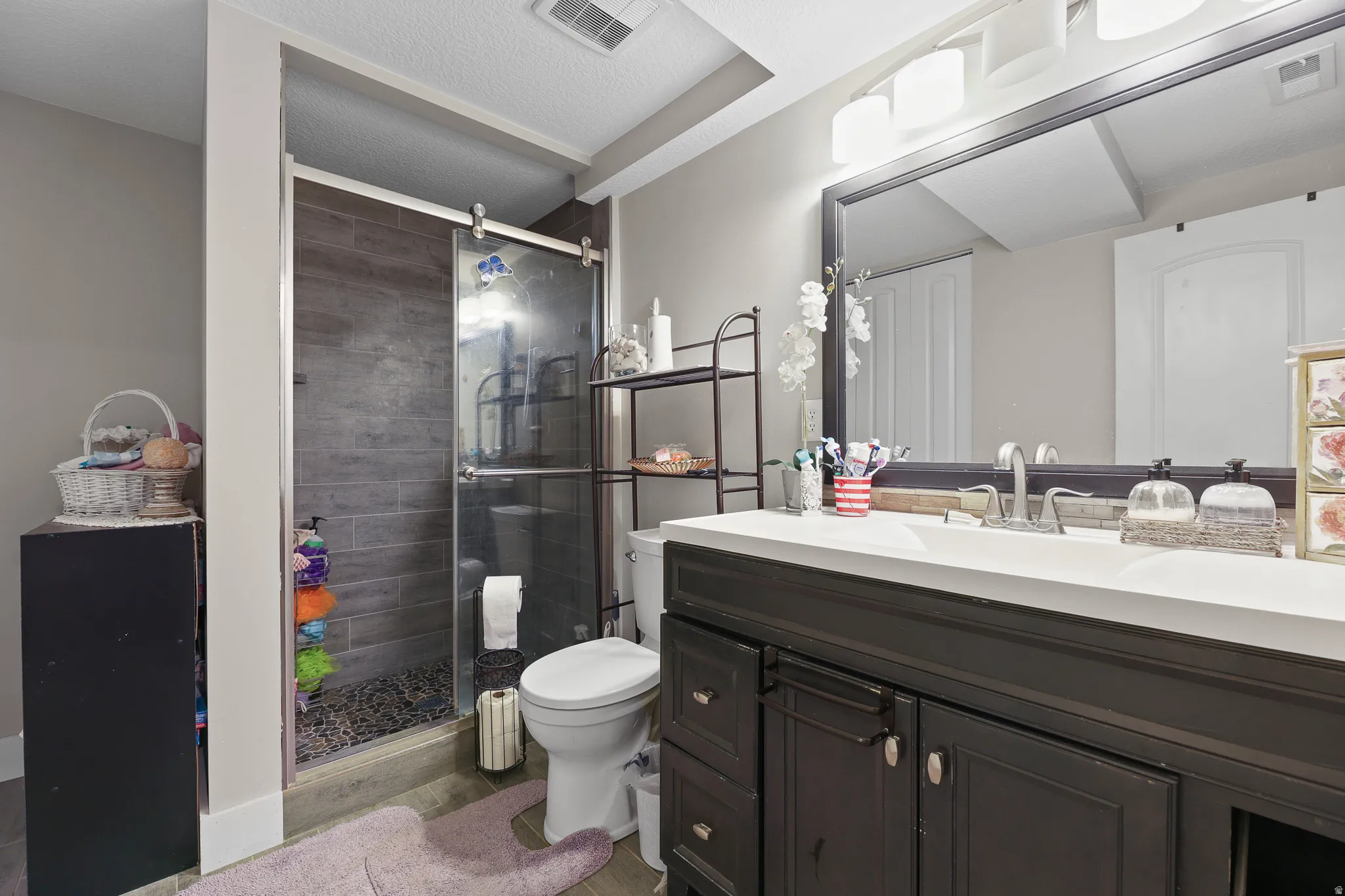 Glass-enclosed shower with dark tile surround and pebble floor