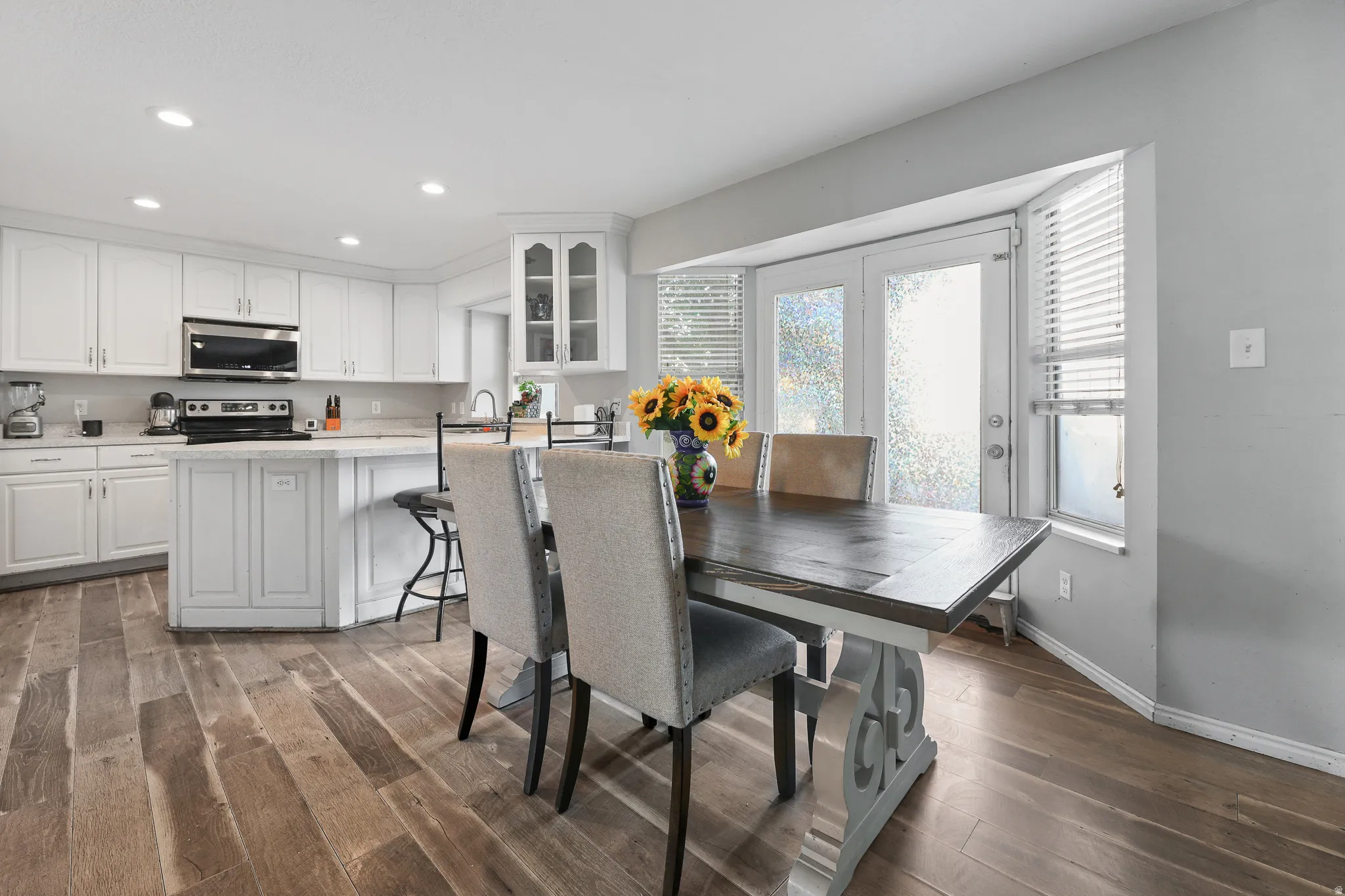 White cabinetry, stainless steel appliances, wood-finish flooring, recessed lighting, and a bay window with double doors