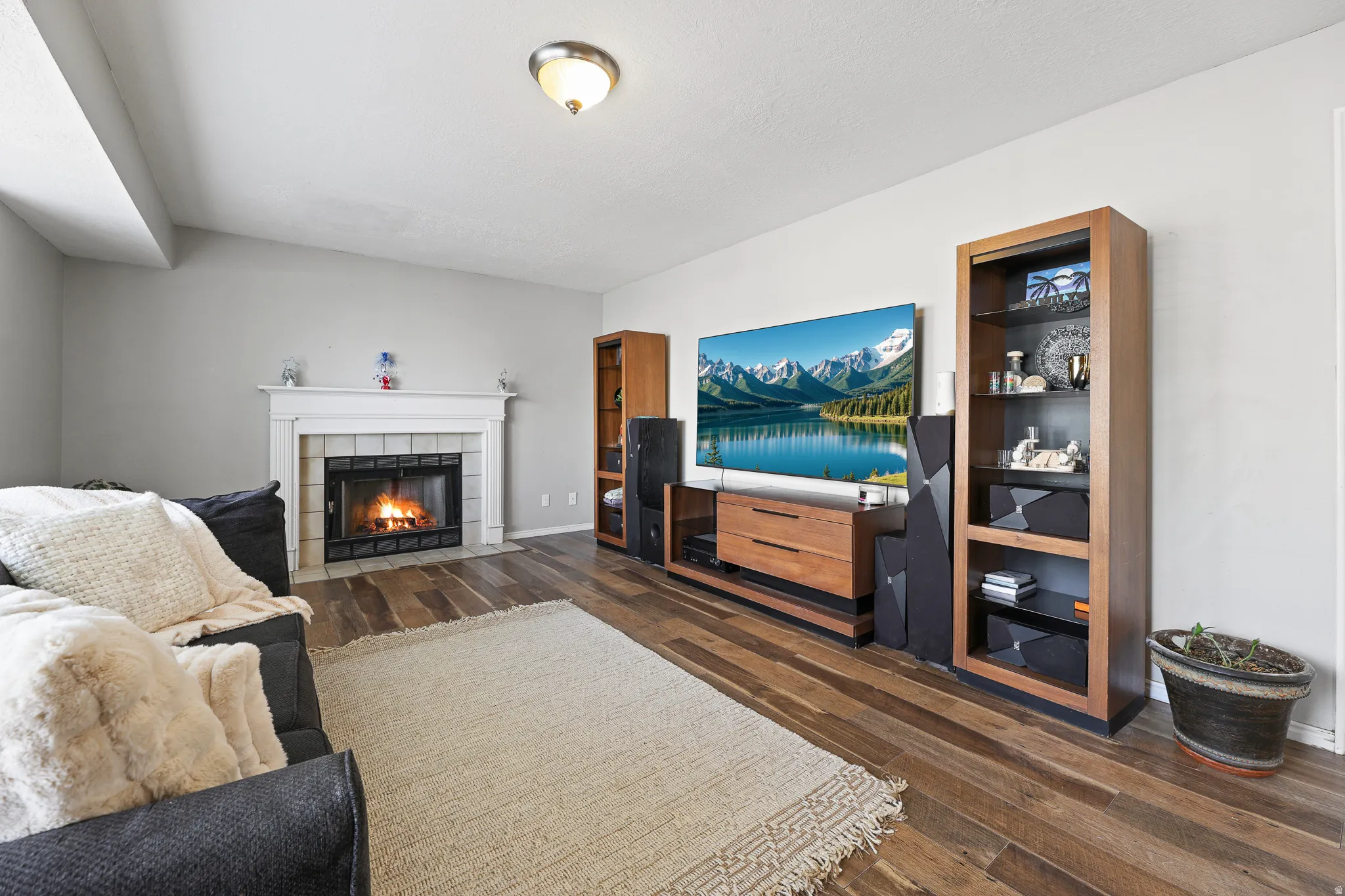 Wood-finish flooring with a fireplace featuring a white mantel and tile surround