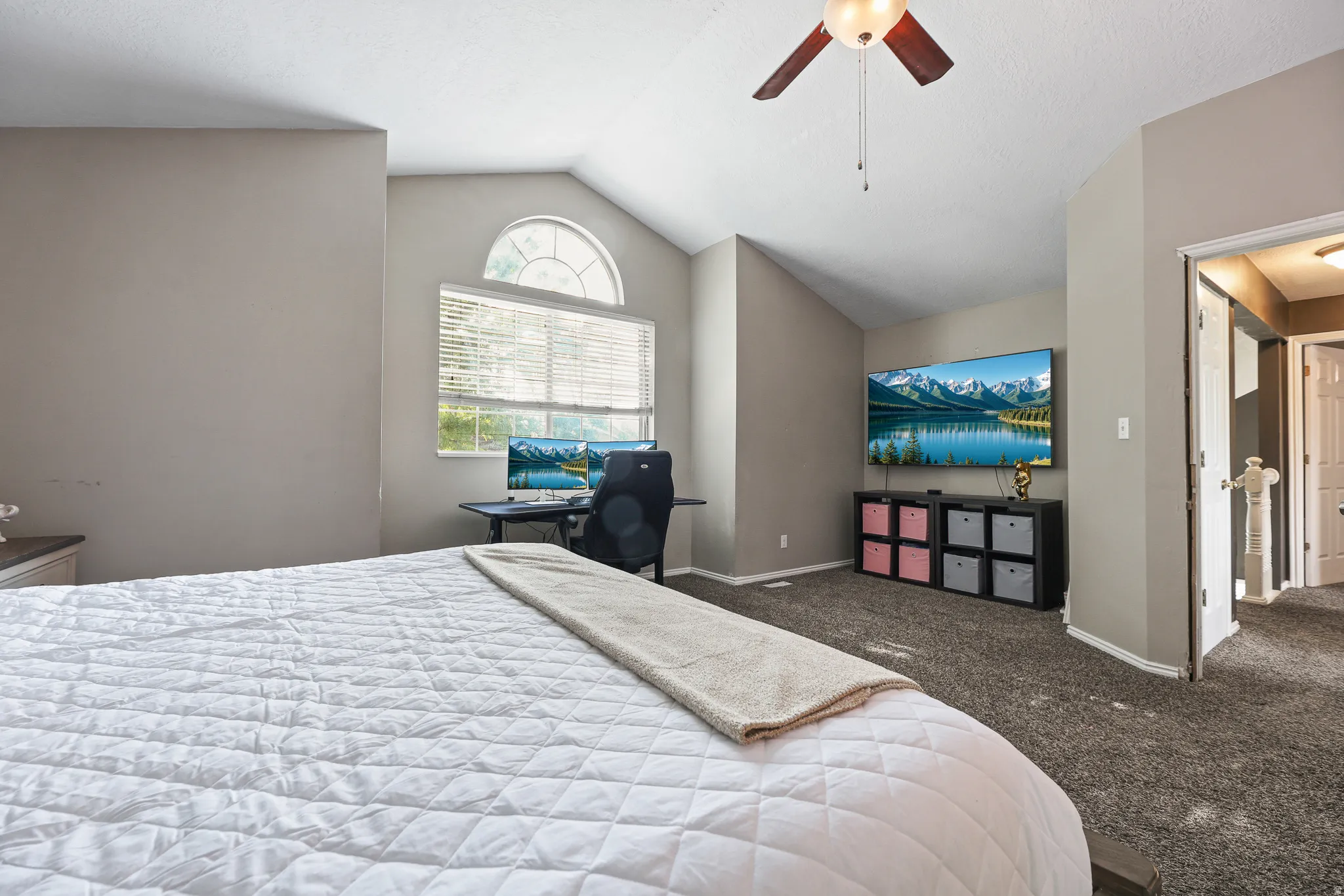 Vaulted ceiling with ceiling fan, arched transom window, and wall-to-wall carpeting