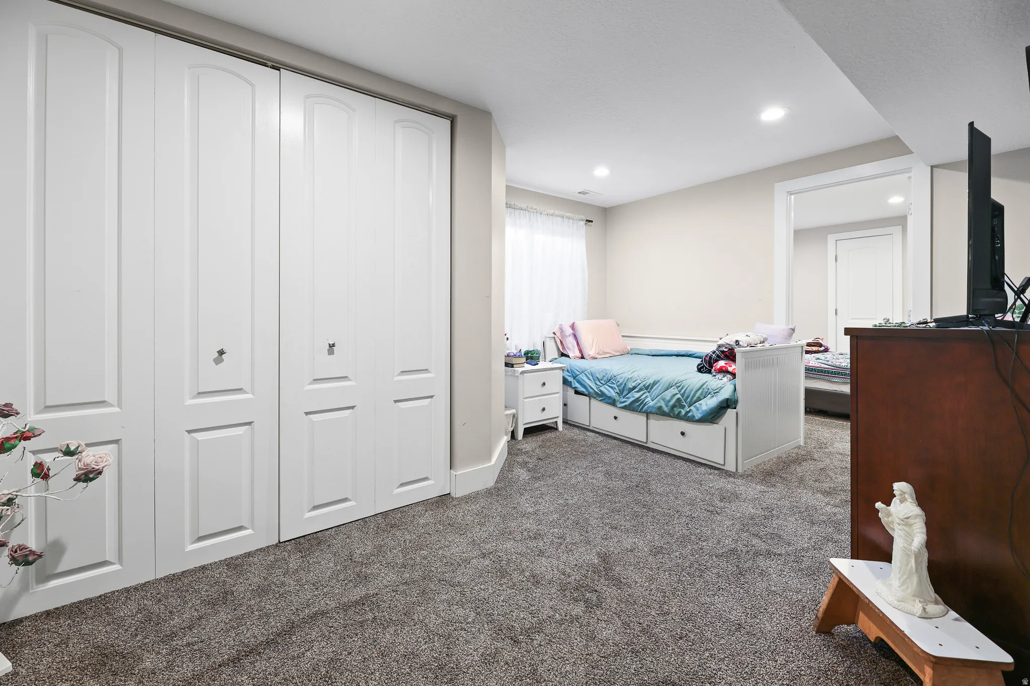 White bi-fold closet doors, recessed ceiling lighting, light-colored walls, and gray carpeting