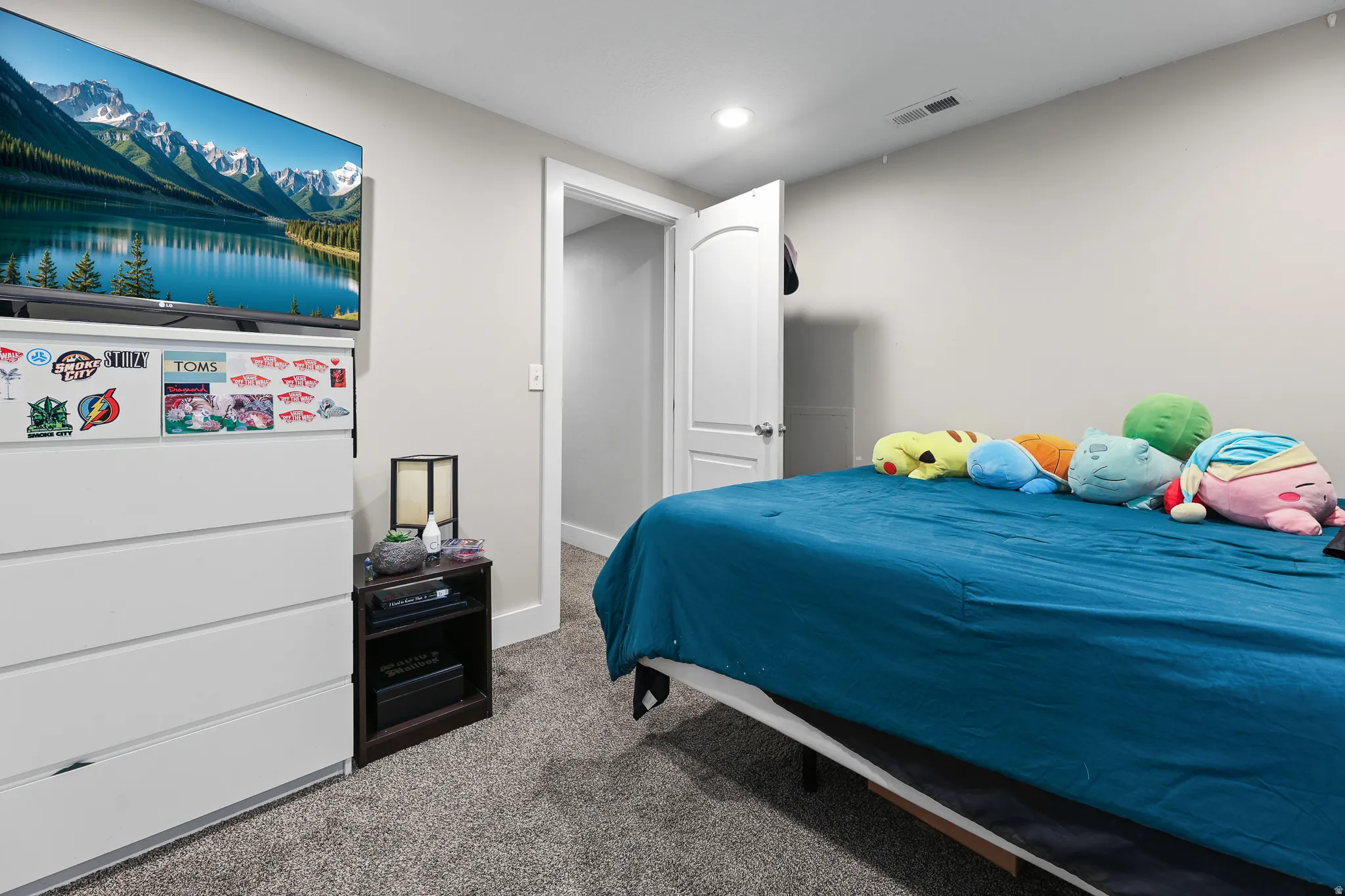 Bright secondary bedroom featuring carpeted flooring, built-in white cabinetry with ample storage, recessed ceiling lighting, and a full-size bed frame with blue bedding