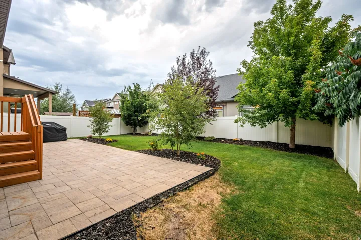 Expansive backyard oasis featuring a paved patio with geometric stone detailing, lush manicured lawn, and mature landscaping with mixed tree plantings