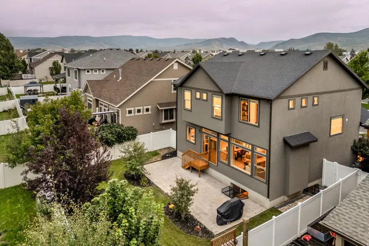 Stucco exterior with a dark shingle roof, complemented by a private backyard featuring a paver patio and established landscaping
