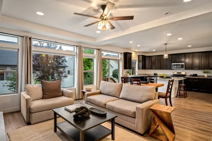 Open-concept living area featuring a coffered ceiling with recessed lighting and ceiling fan, expansive multi-panel sliding glass doors and transom windows flooding the space with natural light, warm wood-finish flooring throughout, and seamless sightline