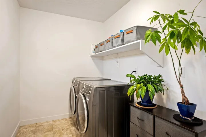 Dedicated laundry room featuring a front-load washer and dryer, floating shelving with decorative storage baskets, tile flooring, and abundant natural light from recessed ceiling fixtures