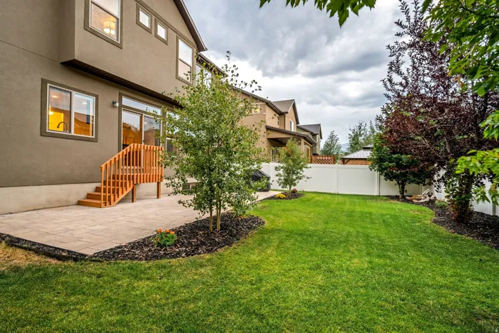 Expansive backyard featuring a manicured lawn, established landscaping, and a paver patio with a wood-finish staircase