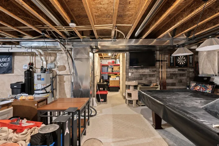 Finished lower level with exposed ceiling joists and ductwork, featuring a dedicated entertainment area with a wall-mounted display, rustic wood-paneled accent wall, and recessed lighting