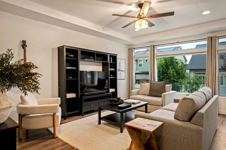 Tray ceiling with recessed lighting, wood-finish flooring, built-in media console, large windows, and a ceiling fan with integrated lighting