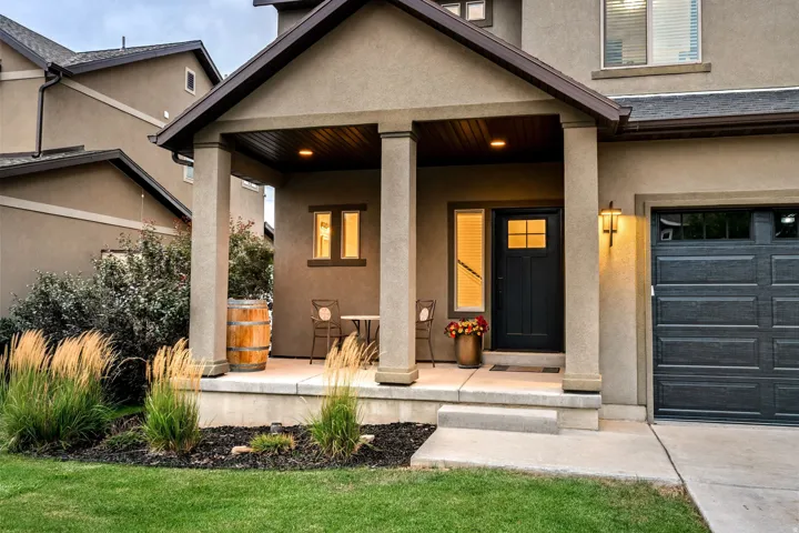 Stucco exterior with a covered porch featuring square columns, a dark panel garage door, a front door with decorative lites, and a concrete pathway