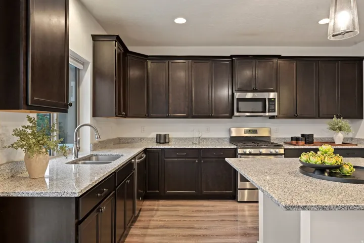 Kitchen featuring dark wood cabinetry, light-toned countertops, stainless steel appliances, a kitchen island, and wood-finish flooring