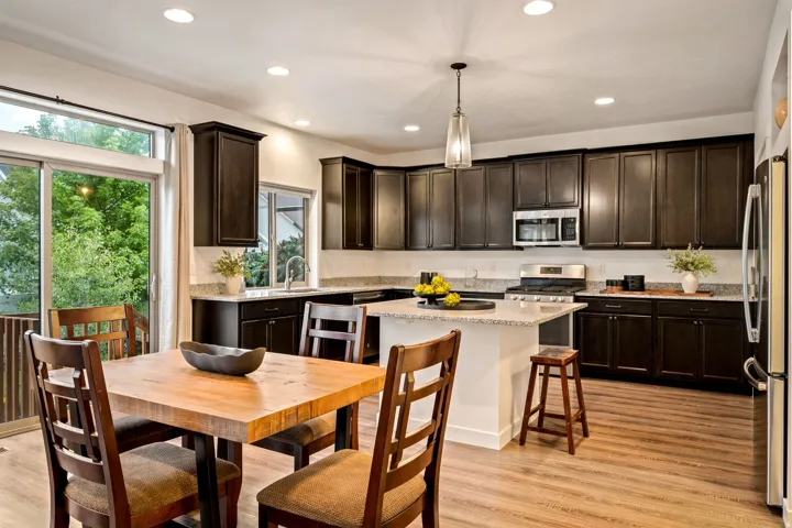 Kitchen featuring dark wood-finish cabinetry, light stone countertops, stainless steel appliances, a center island with pendant lighting, and wood-finish flooring
