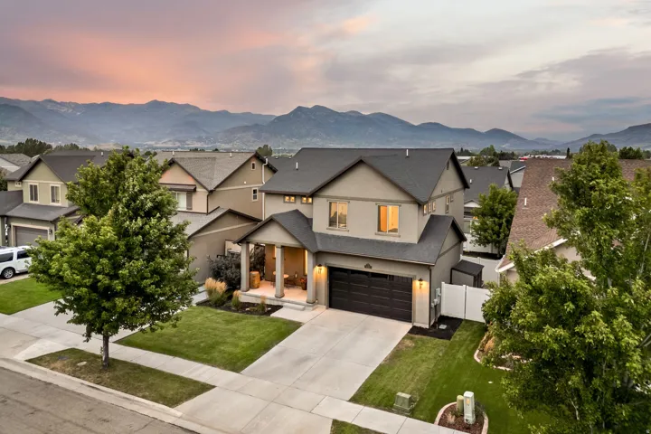 Stucco exterior with a dark shingle roof, attached two-car garage, covered porch with columns, and mature landscaping