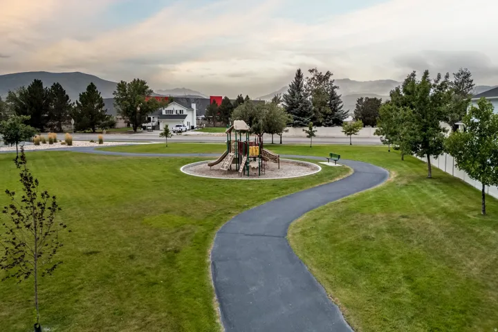 Expansive greenspace featuring a paved walking path, mature trees, and a playground structure