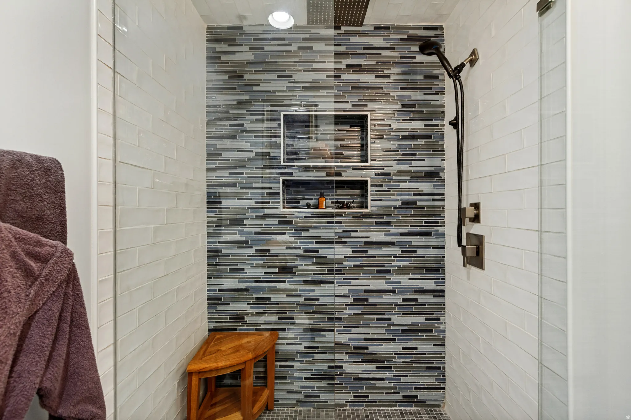 Shower with multi-tone mosaic tile accent wall, built-in recessed shelving, a rainfall showerhead, and a handheld shower fixture