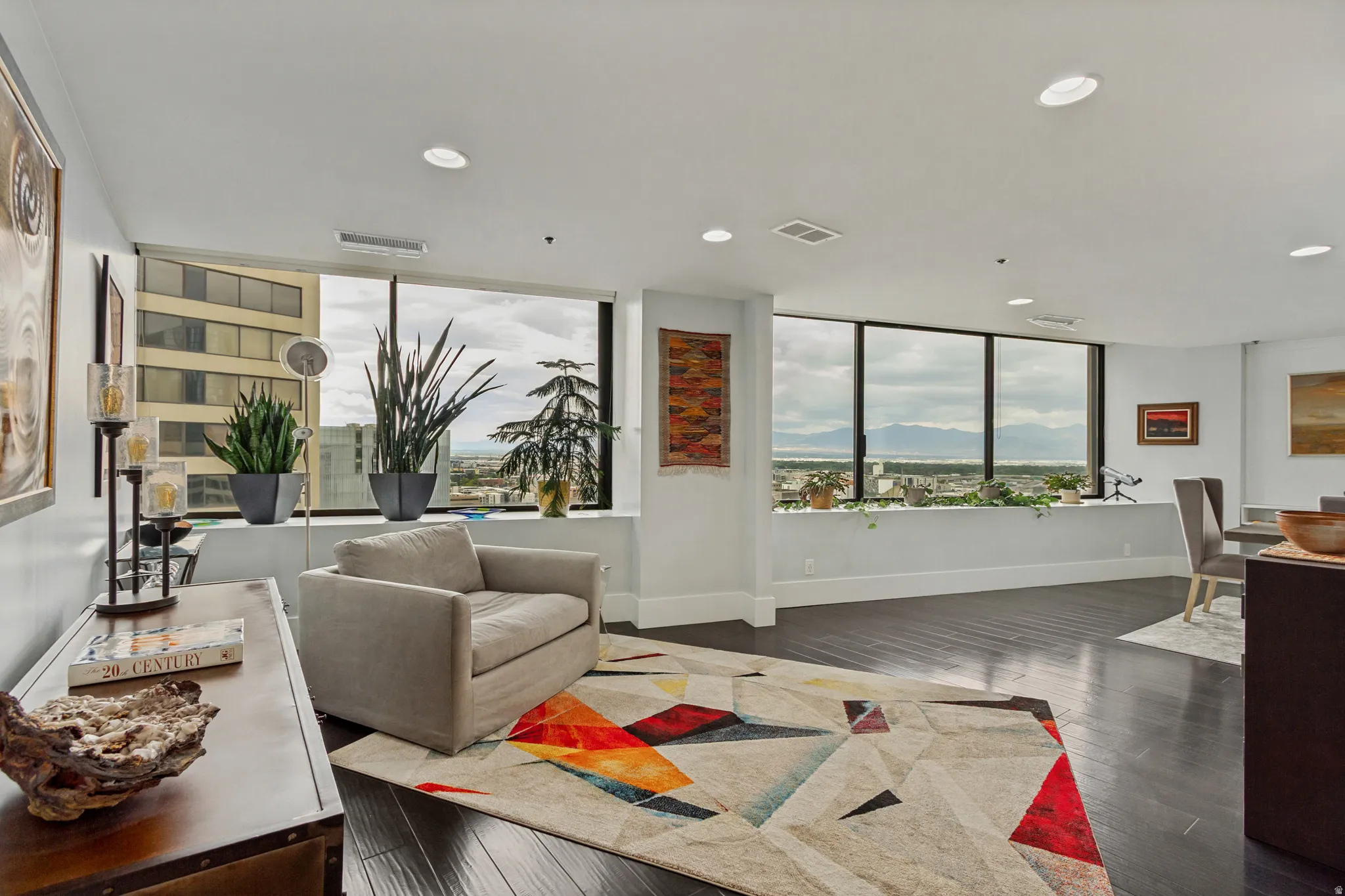 Expansive window wall with mountain and urban scenery, dark wood-finish flooring, recessed lighting, and white baseboards
