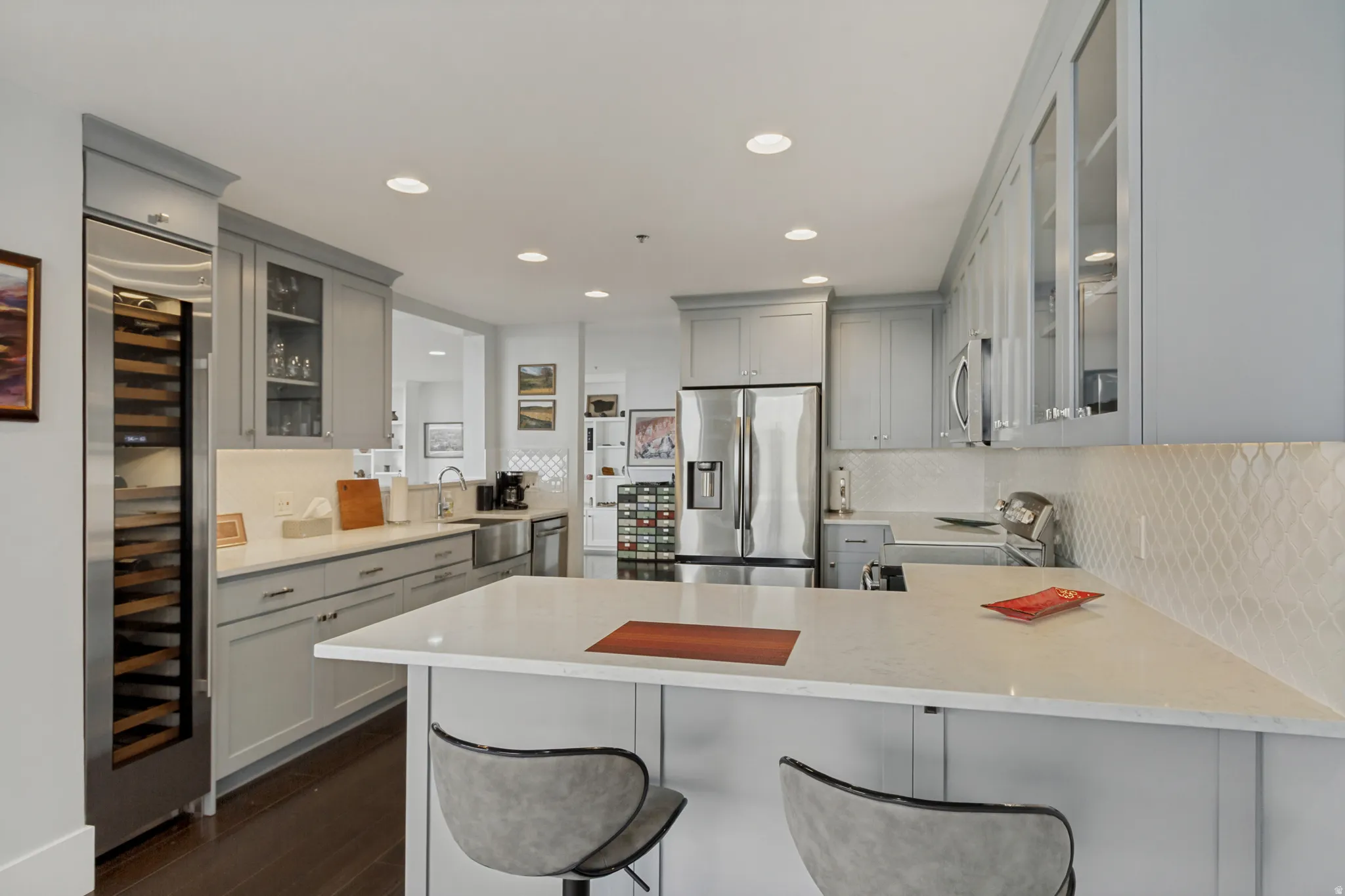 Modern kitchen with light gray cabinetry, stainless steel appliances, a built-in wine refrigerator, white countertops, and a textured backsplash