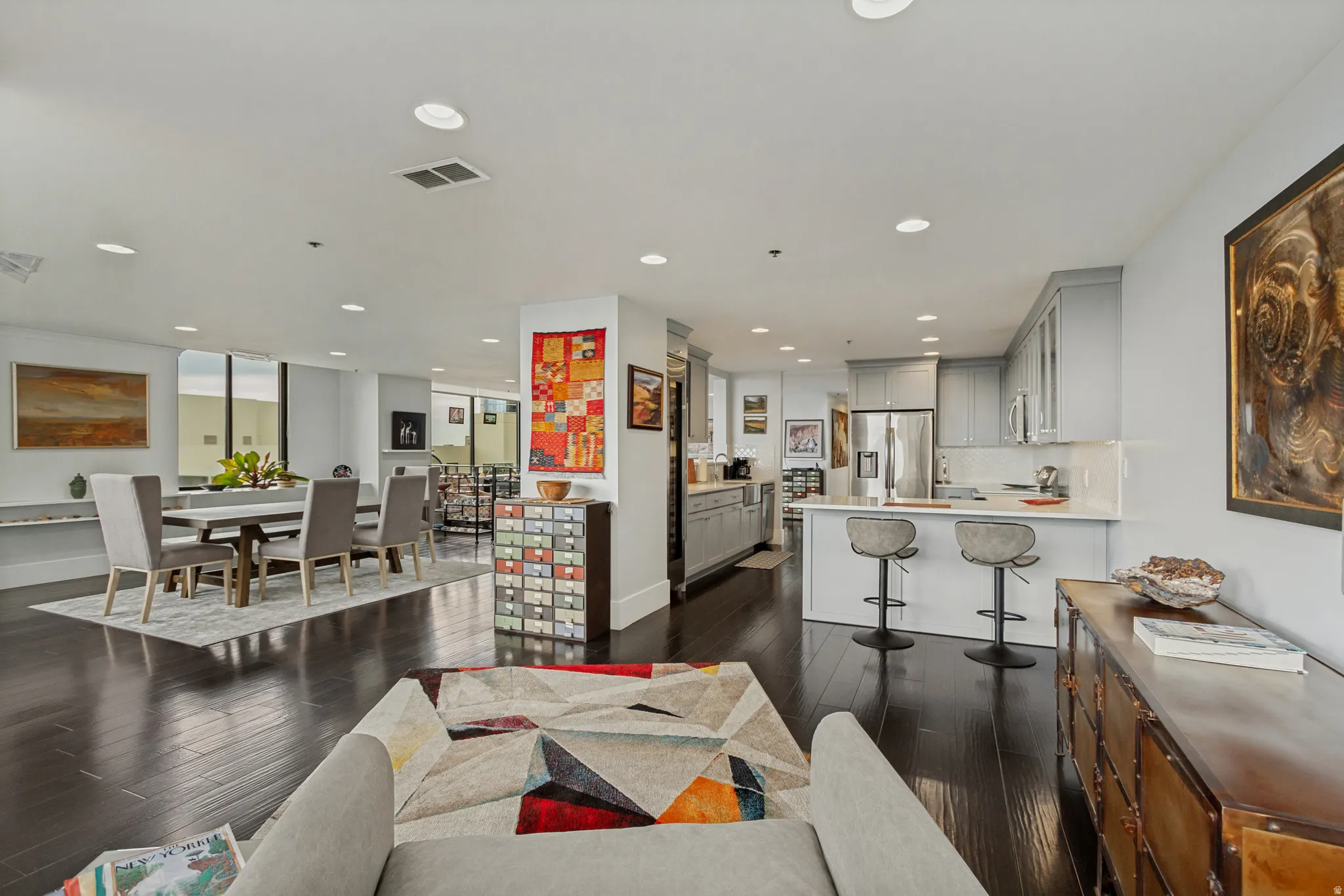 Open-concept living space featuring dark wood-finish flooring throughout, recessed ceiling lighting, and seamless integration of kitchen, dining, and living areas
