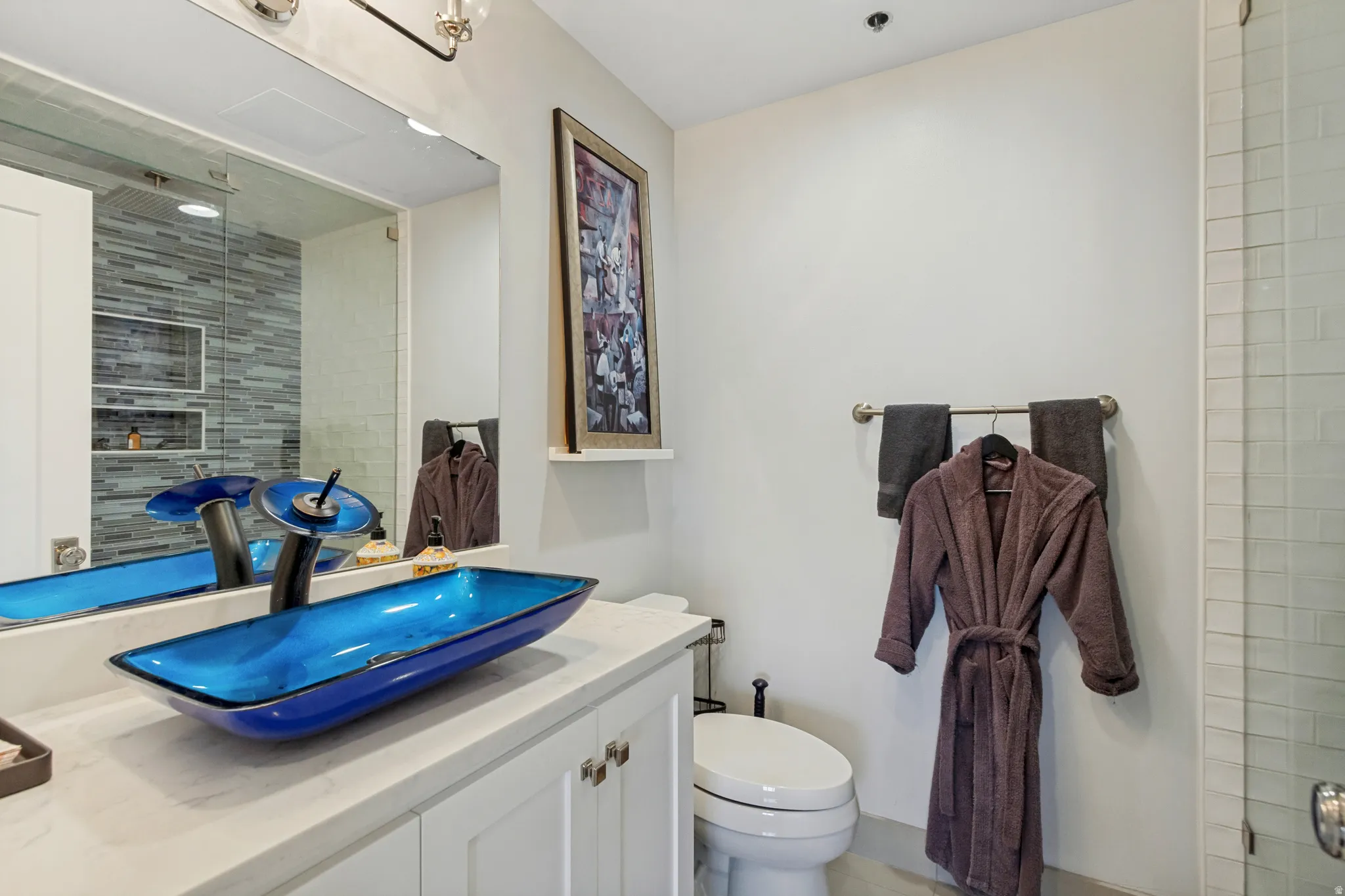 White vanity with brushed nickel hardware, a blue vessel sink, and a waterfall faucet