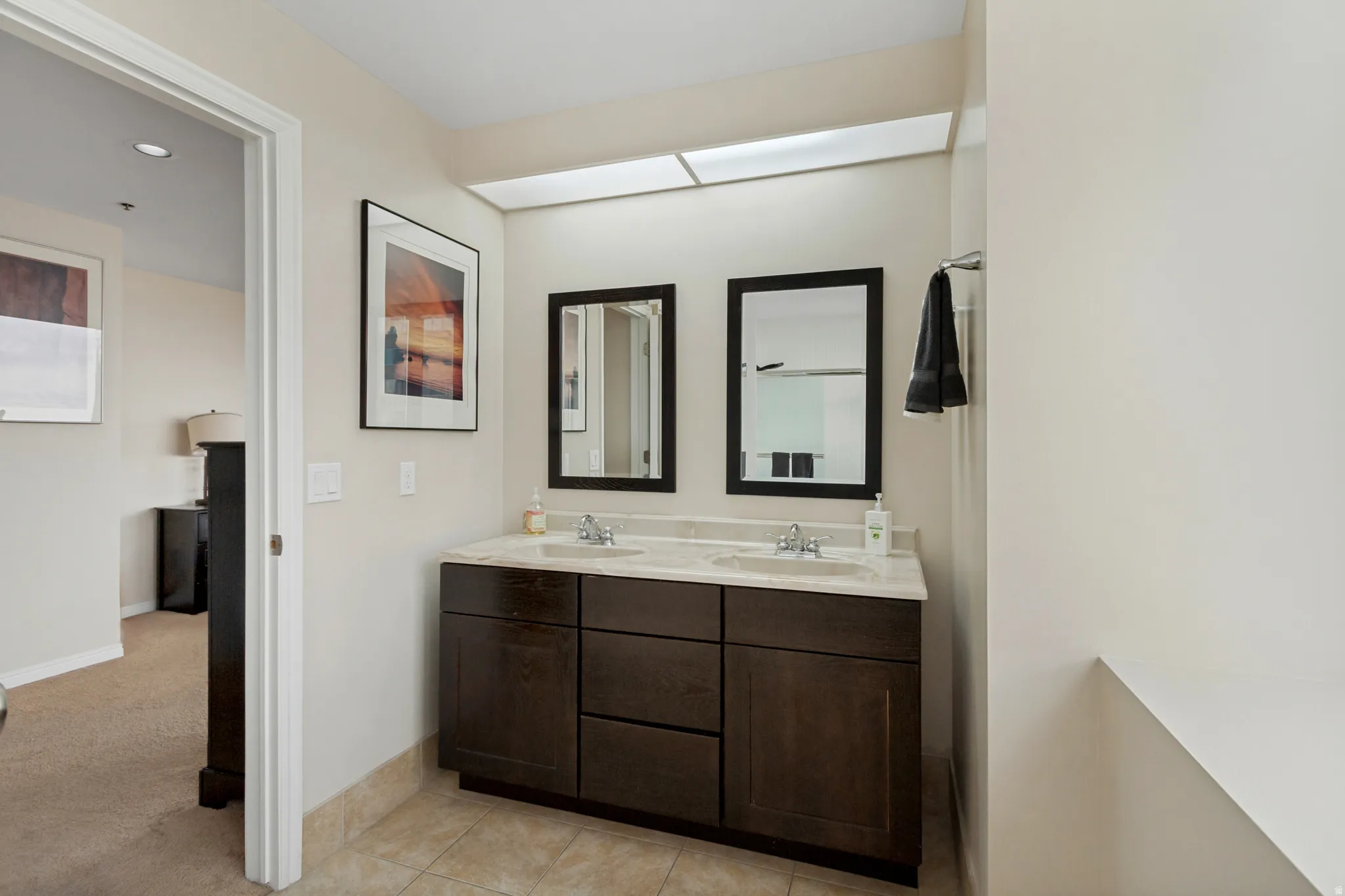 Double vanity with integrated sinks, stone countertop, dark wood-finish cabinetry, and framed mirrors