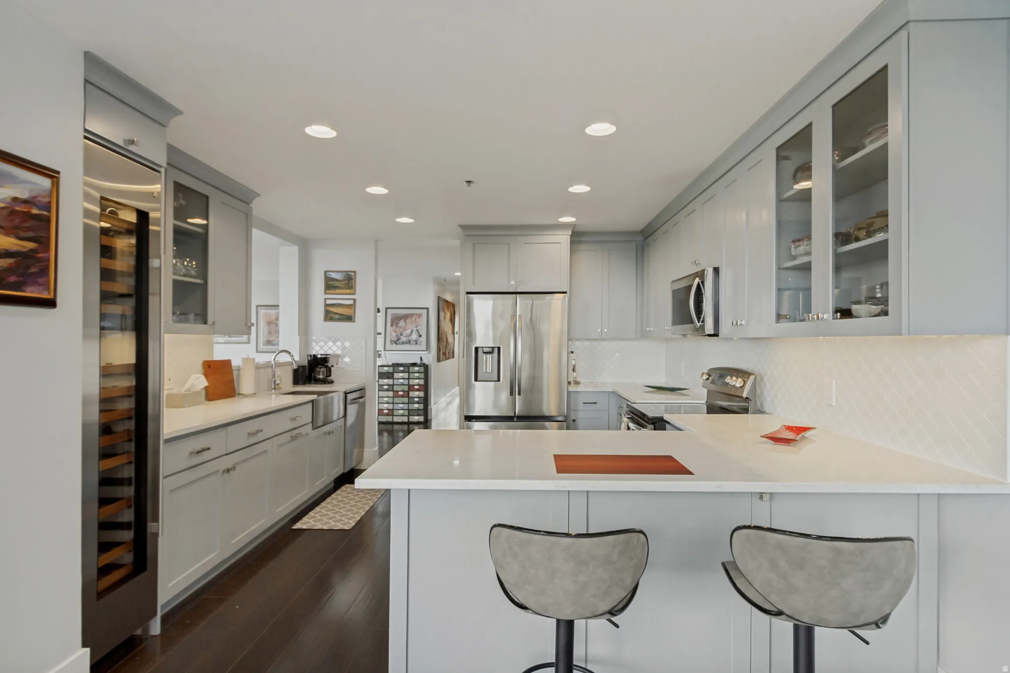 Light gray cabinetry with glass-front upper cabinets, stainless steel appliances, a built-in wine refrigerator, white countertops, and a white diamond-pattern backsplash