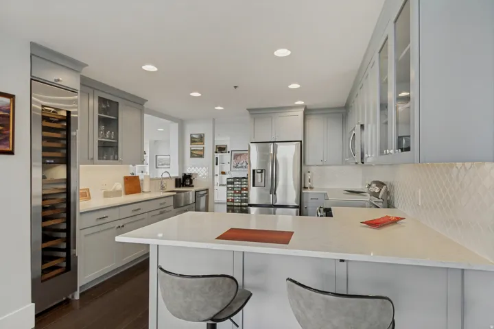 Modern kitchen with light gray cabinetry, stainless steel appliances, a built-in wine refrigerator, white countertops, and a textured backsplash