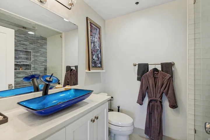White vanity with brushed nickel hardware, a blue vessel sink, and a waterfall faucet