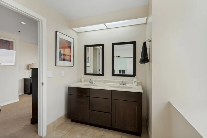Double vanity with integrated sinks, stone countertop, dark wood-finish cabinetry, and framed mirrors