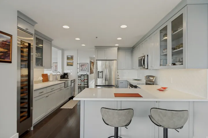 Light gray cabinetry with glass-front upper cabinets, stainless steel appliances, a built-in wine refrigerator, white countertops, and a white diamond-pattern backsplash