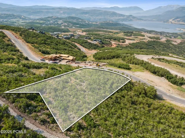 Expansive land parcel with surrounding paved roads, abundant natural greenery, and distant mountain vistas