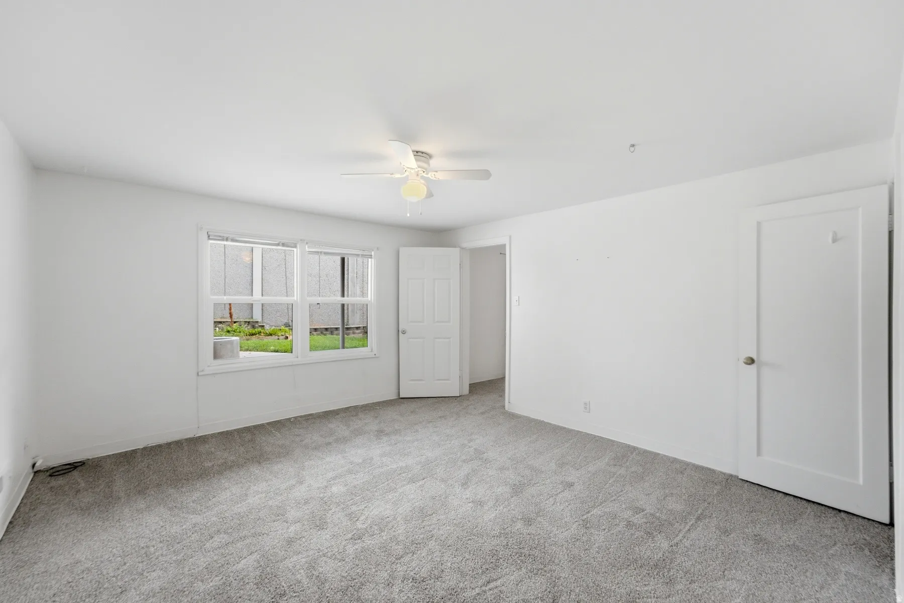 Spacious room featuring neutral carpeting, white walls, a ceiling fan, and a double window