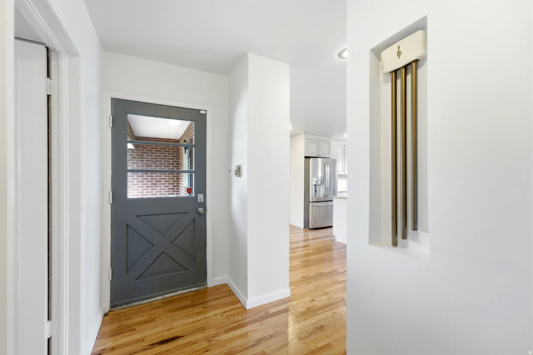 Hardwood flooring, crisp white walls, recessed ceiling lighting, and a partially visible kitchen with stainless steel appliances