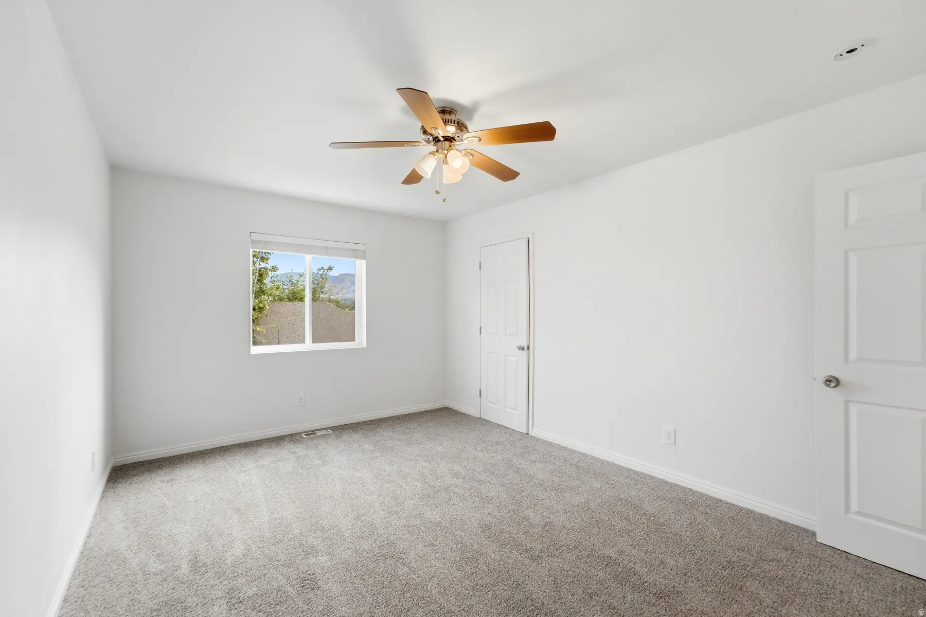 Neutral paint throughout with a ceiling fan, window, and grey carpet flooring