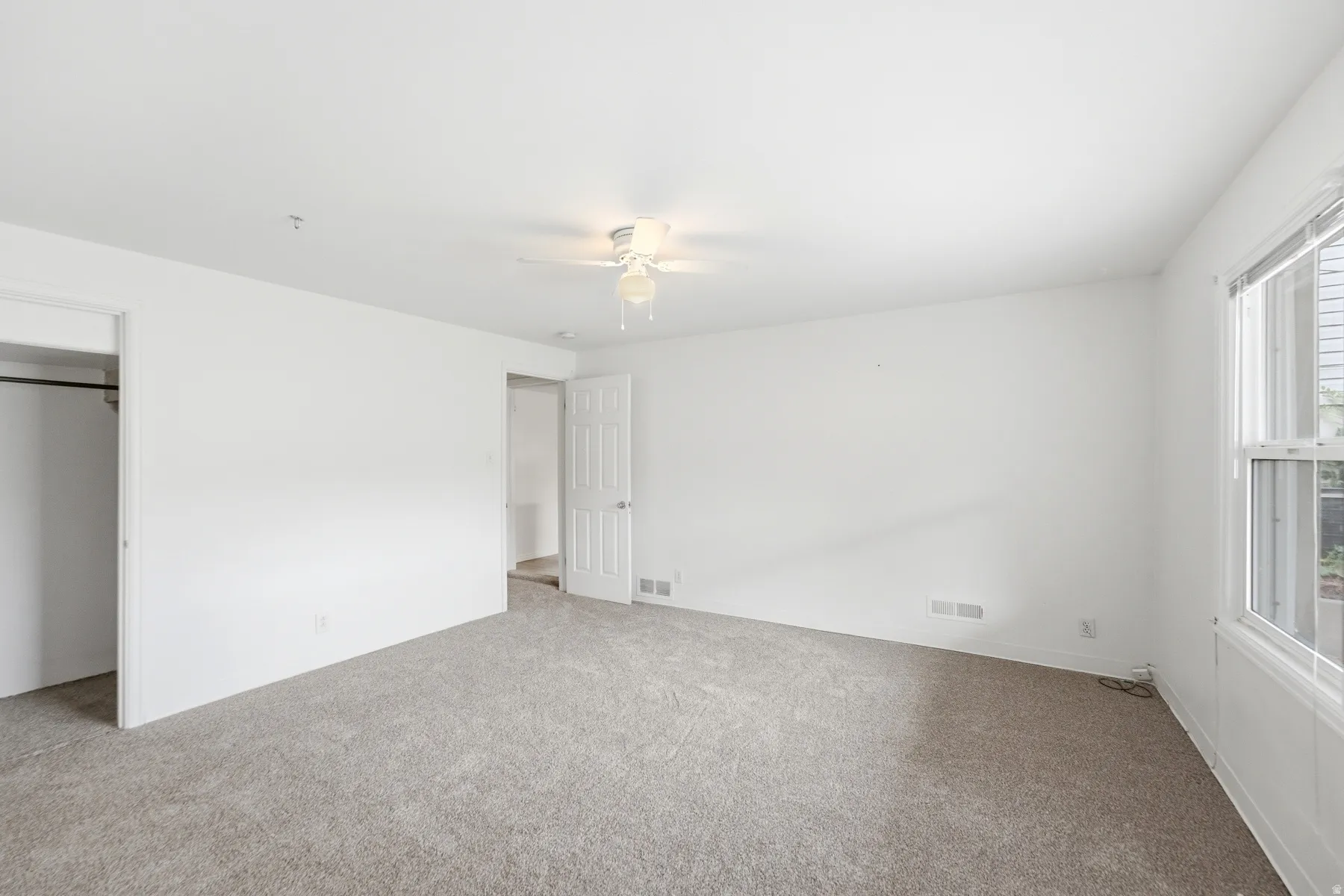 Spacious room featuring light-colored carpeting, white painted walls, a ceiling fan, and a window with white trim