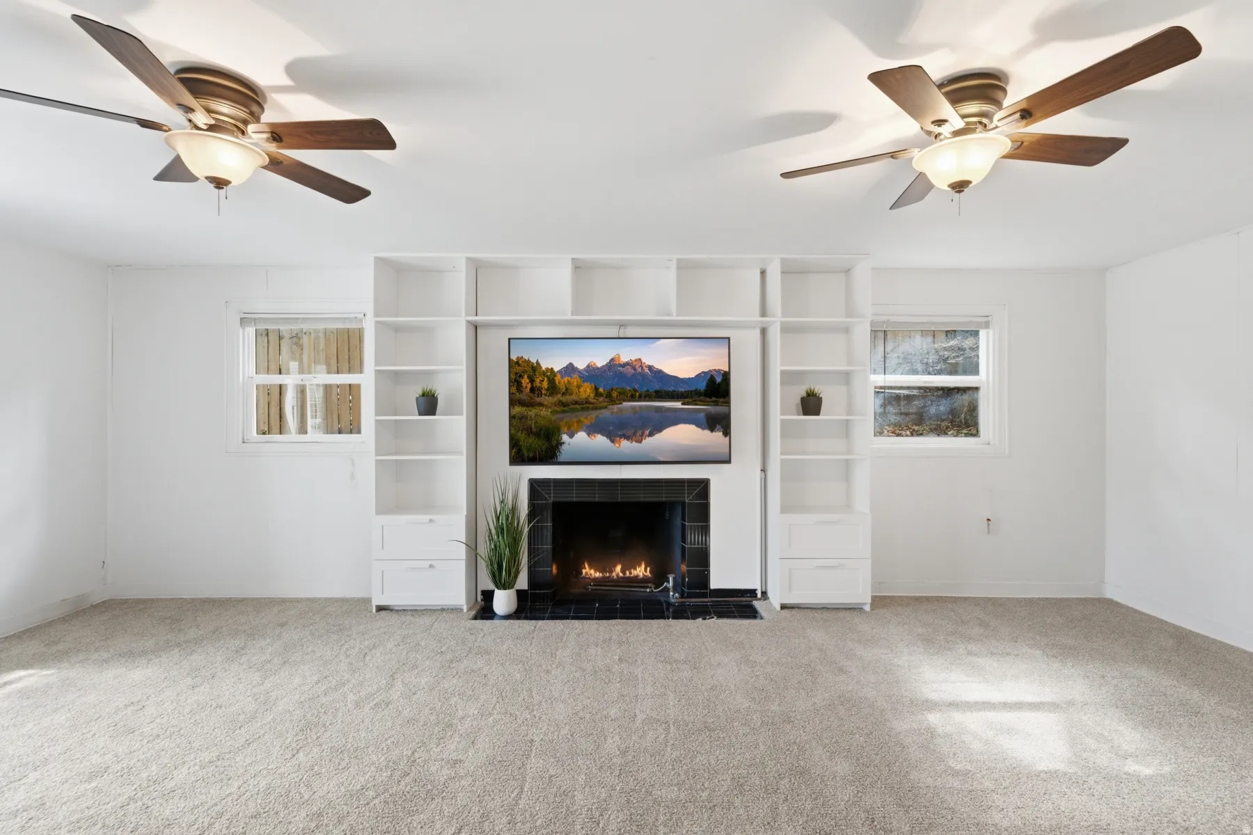 Built-in shelving with integrated media space, modern fireplace with dark tile surround, and two ceiling fans with integrated lighting