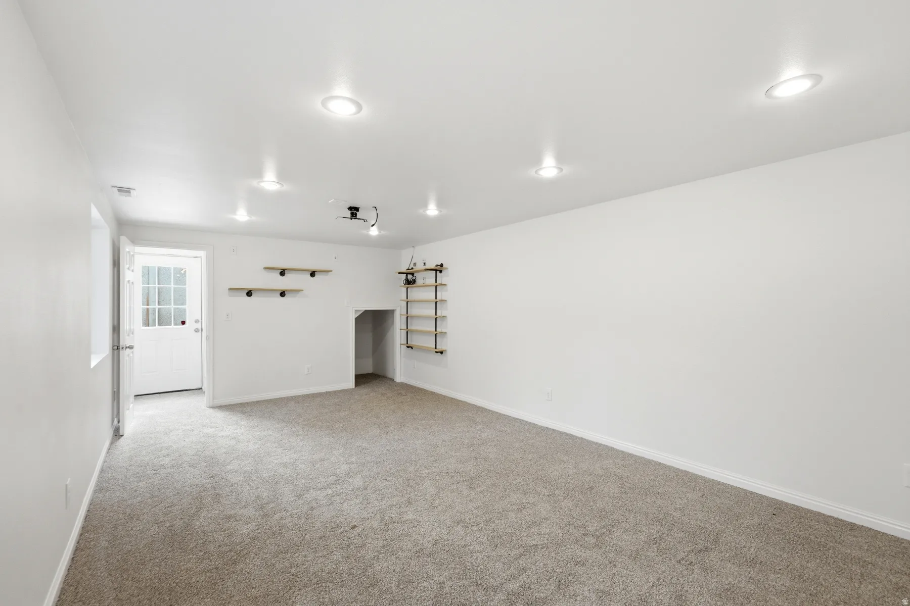 Recessed ceiling lighting, light-toned carpet flooring, built-in shelving, glass-paned door, and a built-in alcove