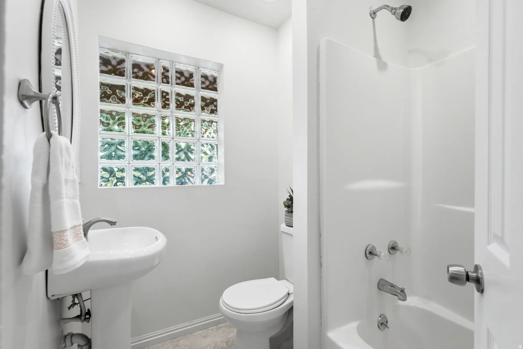 Pedestal sink, glass block window, white toilet, and tub/shower combination