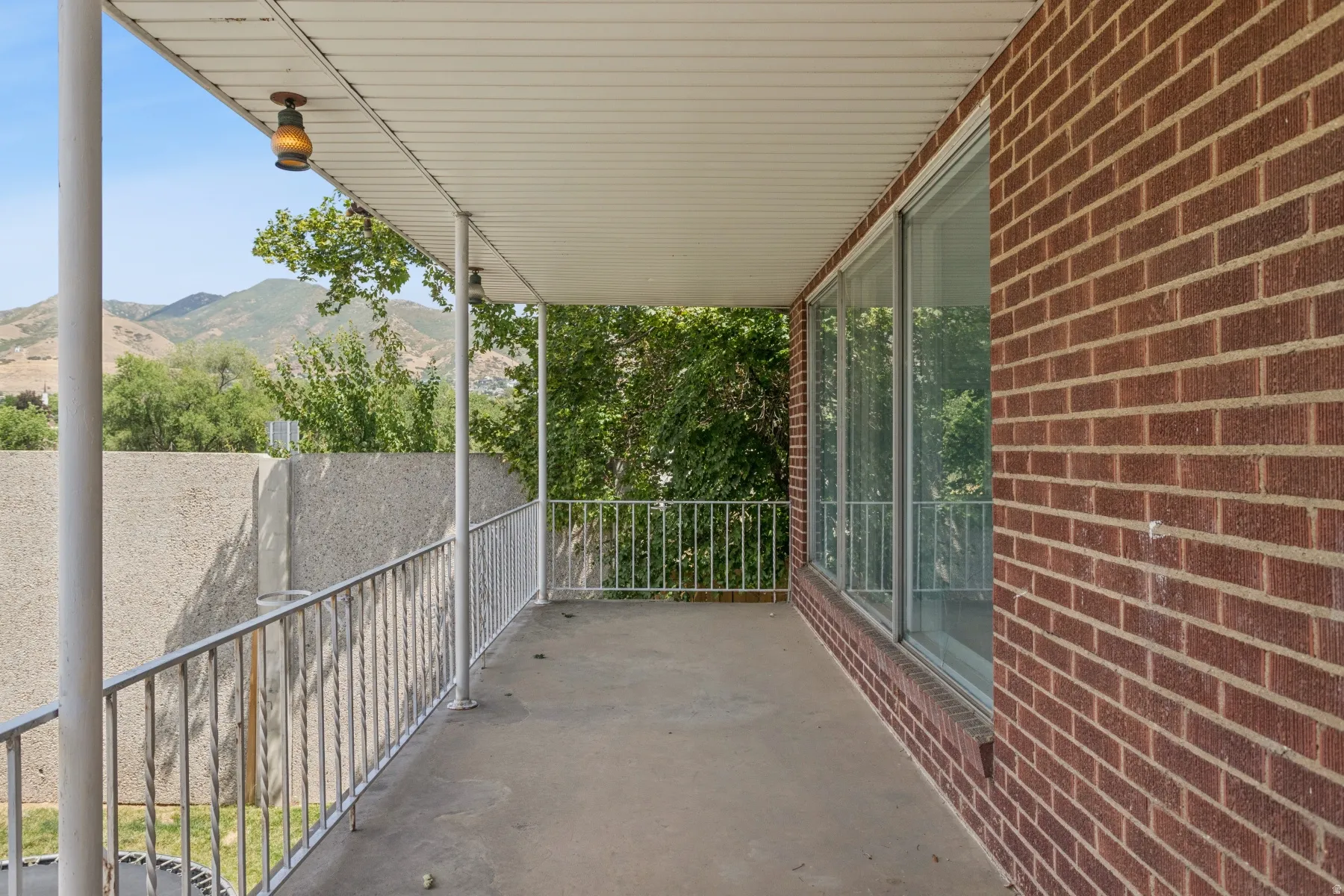 Covered balcony with concrete flooring, white metal railings, and a brick exterior wall