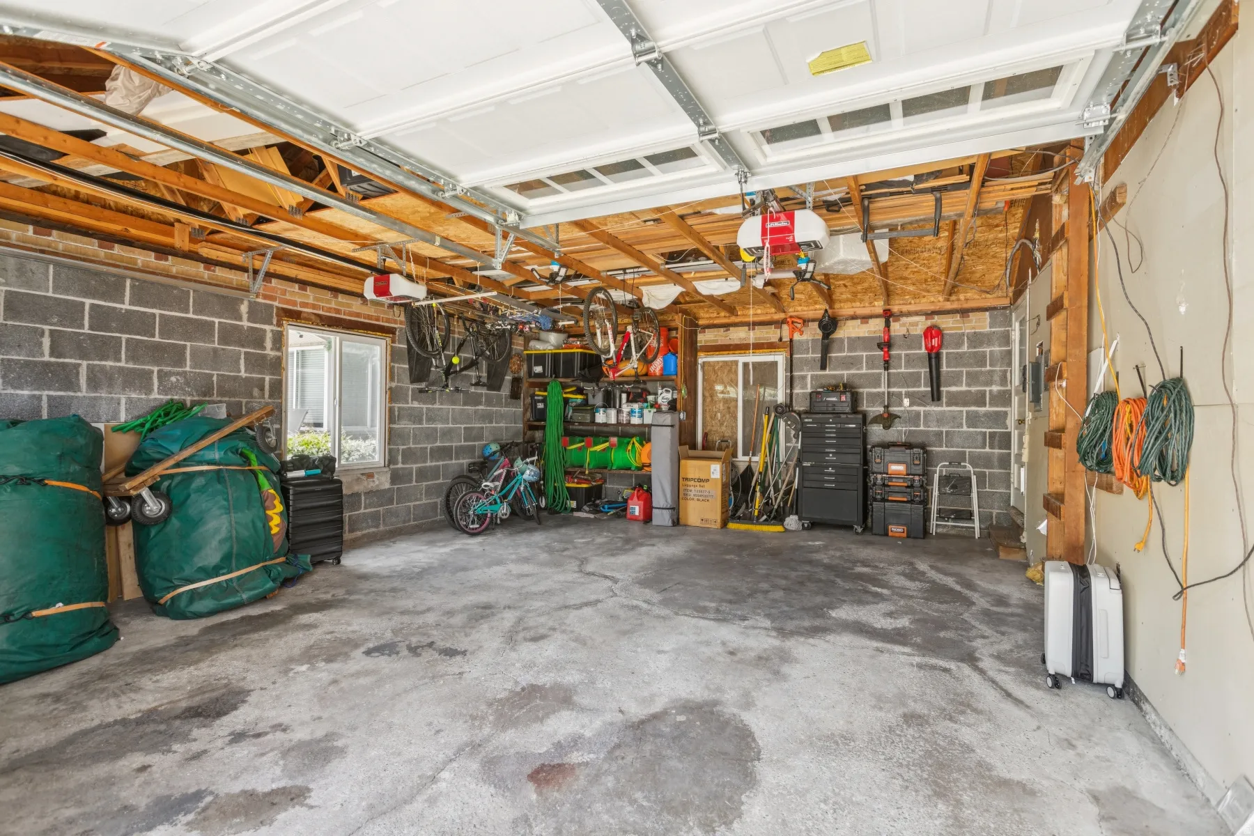 Spacious garage with exposed wood ceiling joists, durable concrete block walls, a concrete floor, and integrated window