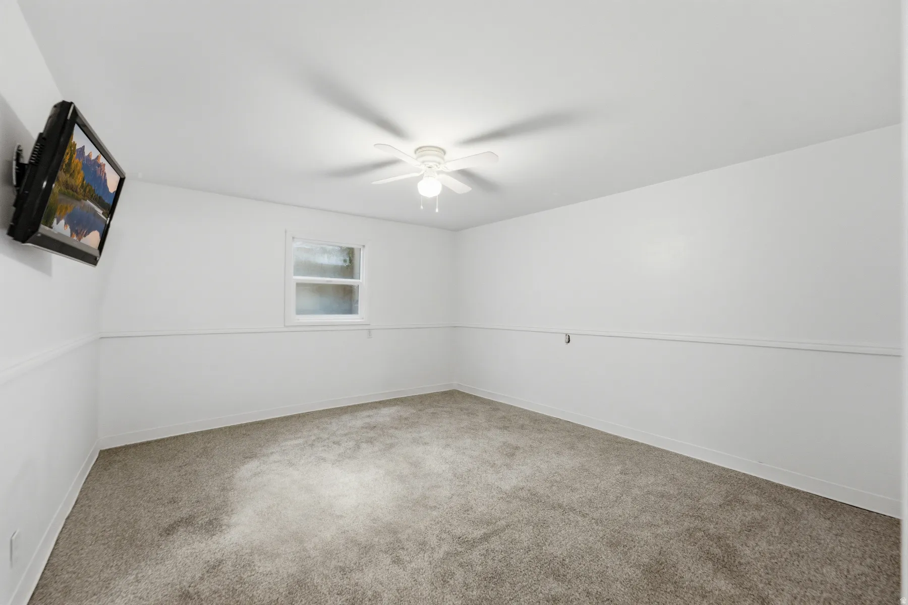 Carpeted interior space featuring a window, ceiling fan with light fixture, and white wall paneling