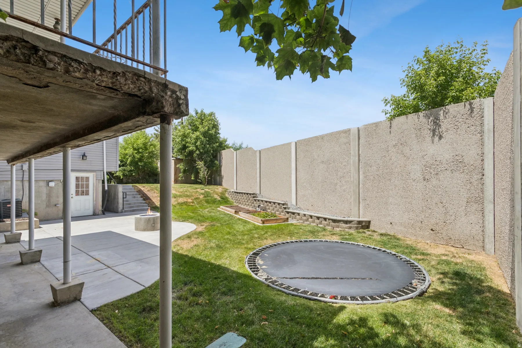 Expansive backyard featuring a concrete patio, a built-in fire pit, and a retaining wall