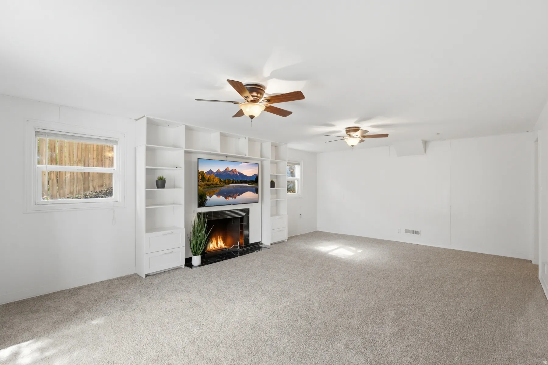 Built-in entertainment center with integrated shelving and drawers, fireplace with a black surround, dual ceiling fans, and neutral carpeting