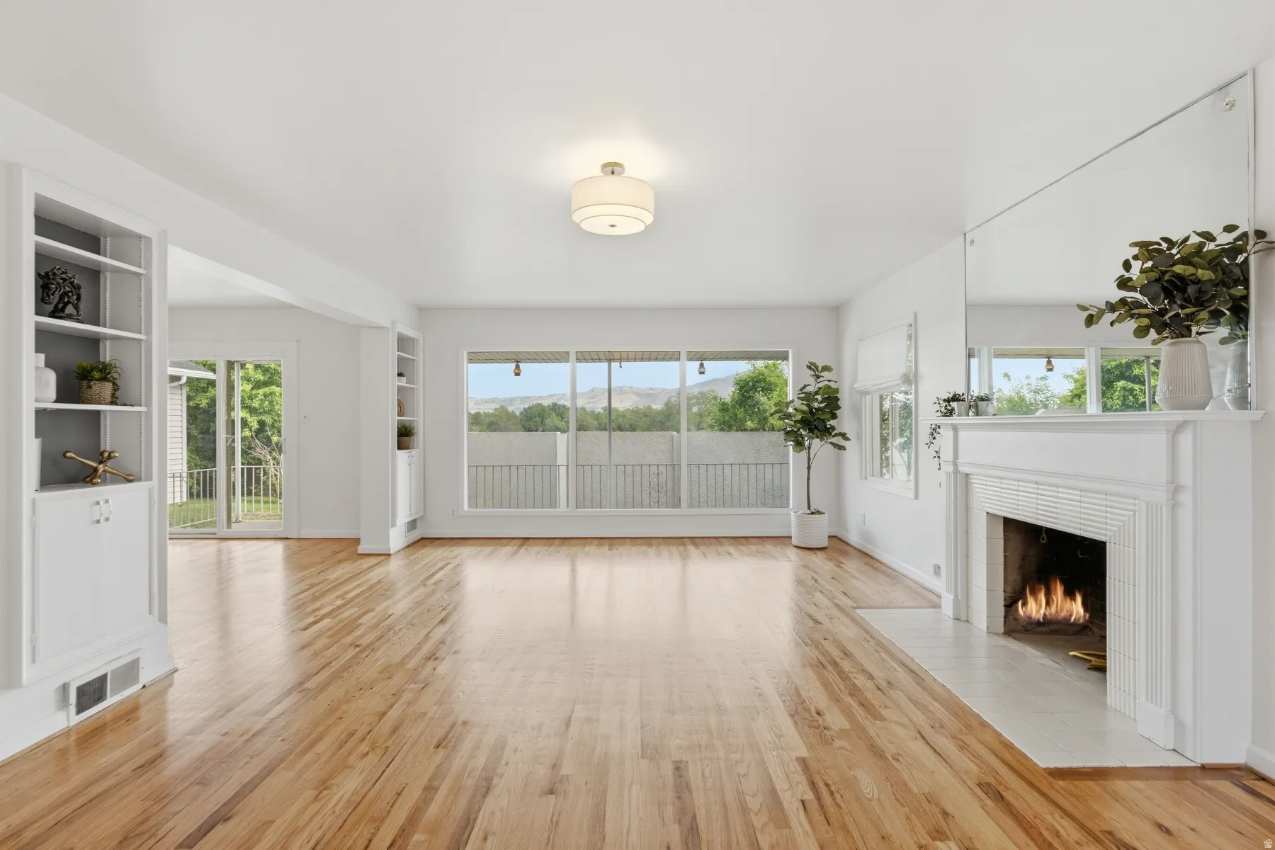 Hardwood flooring throughout, built-in shelving, white fireplace with tile hearth, large picture windows, and recessed lighting