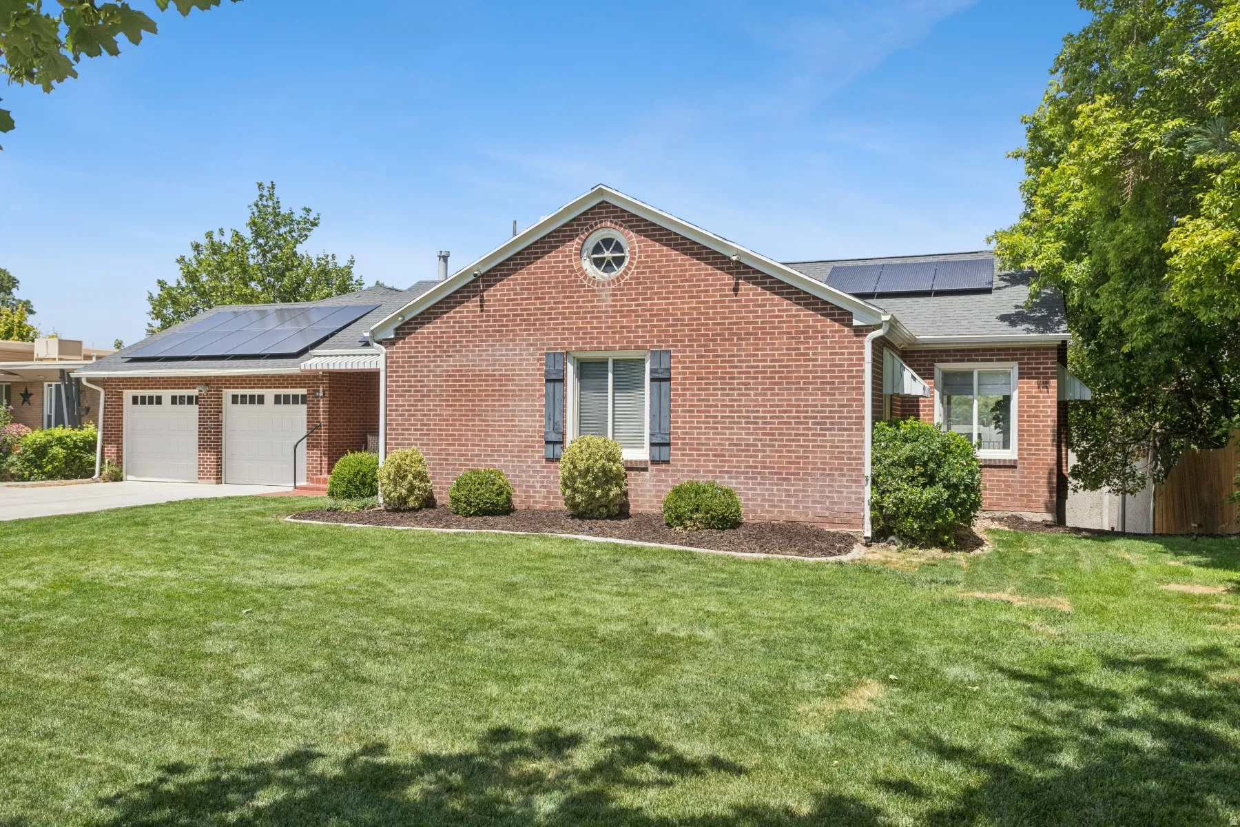 Brick Colonial home featuring a two-car attached garage, manicured front lawn with mature landscaping, and a gable roof with architectural detailing