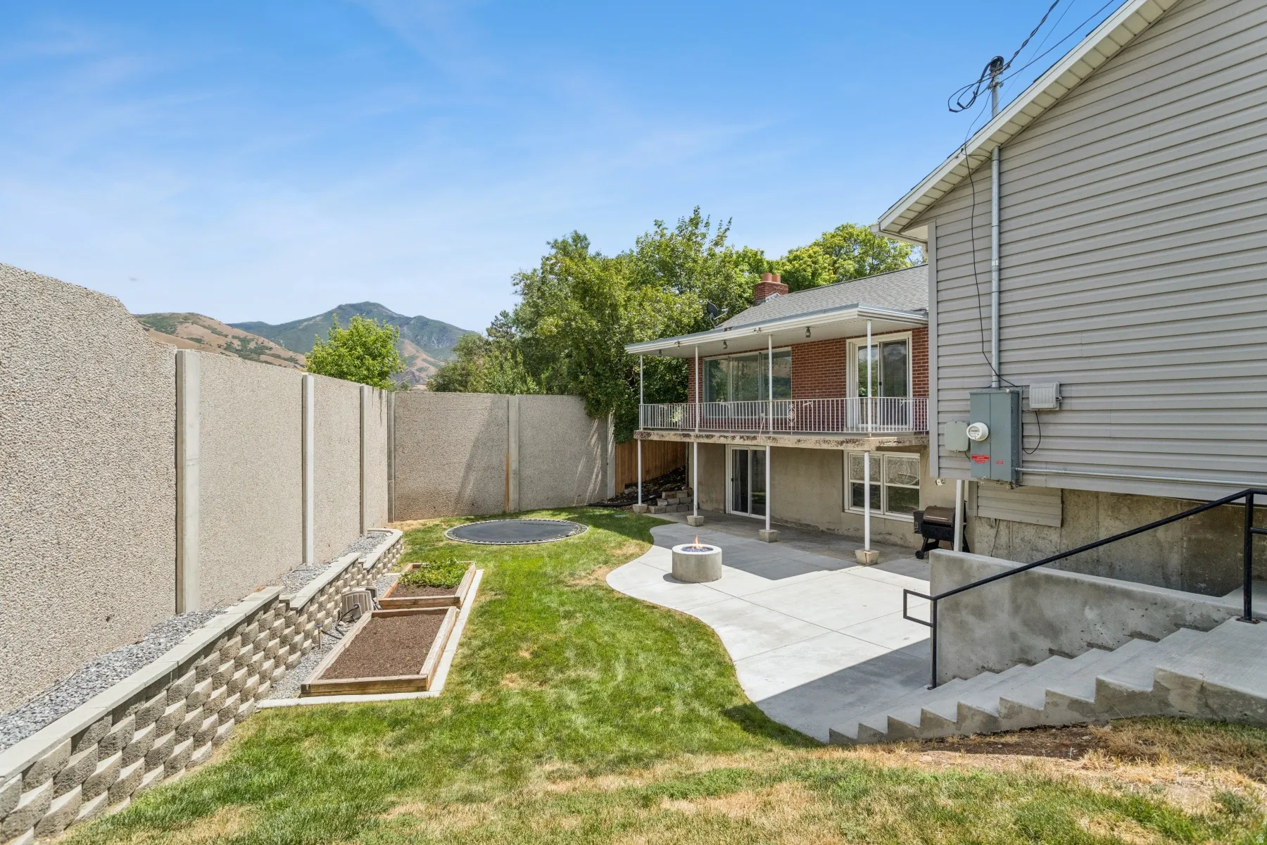 Expansive backyard featuring a concrete patio, built-in fire pit, terraced retaining wall, and a concrete perimeter fence