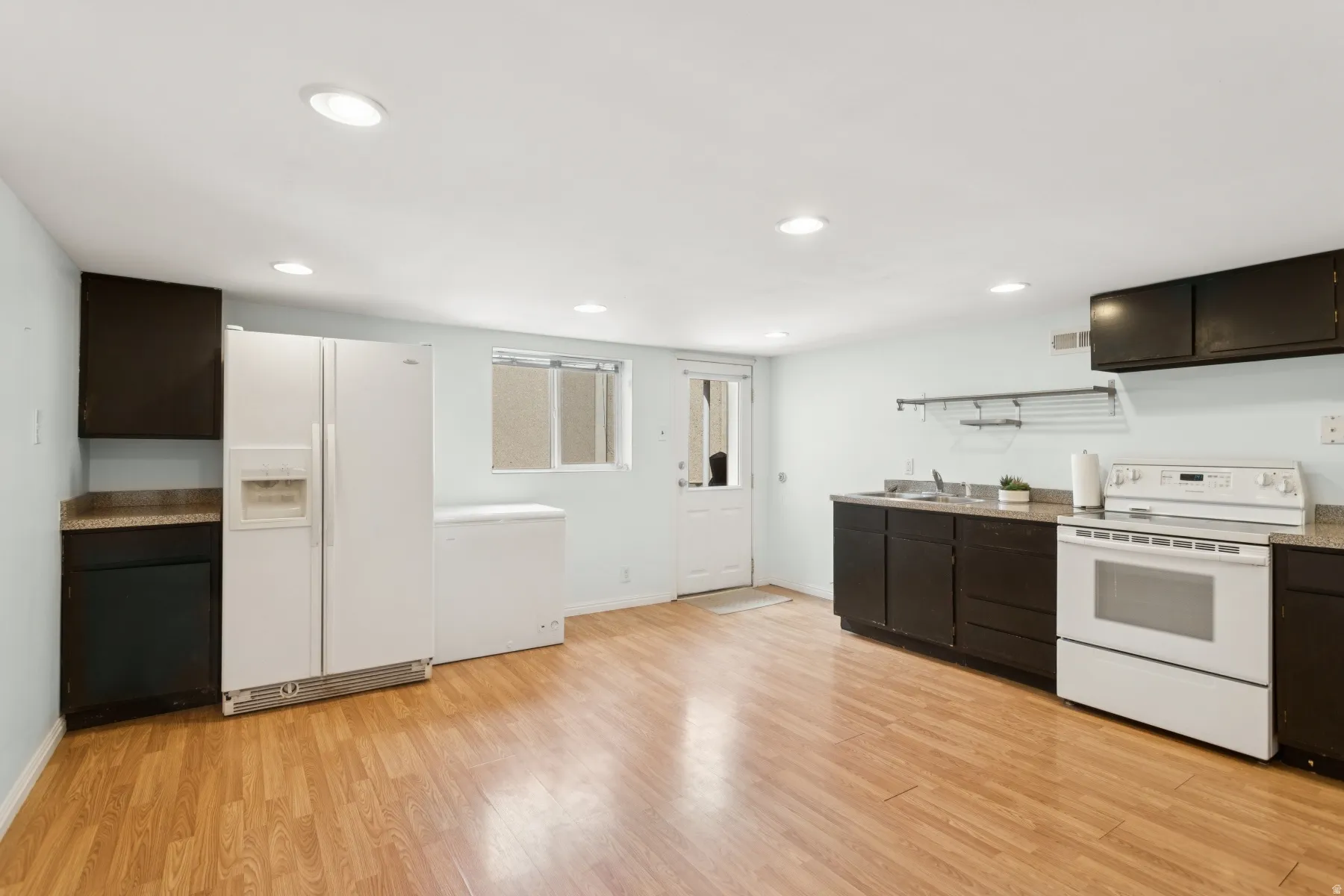 Kitchen area featuring wood-finish flooring, dark cabinetry, and light-colored countertops